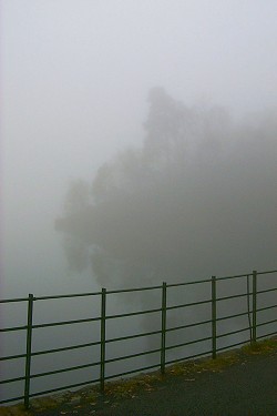 Picture of a rail along a road with an island in a loch in the background just visible in the fog