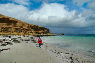 Picture of a few walkers on a beach, approaching a hill